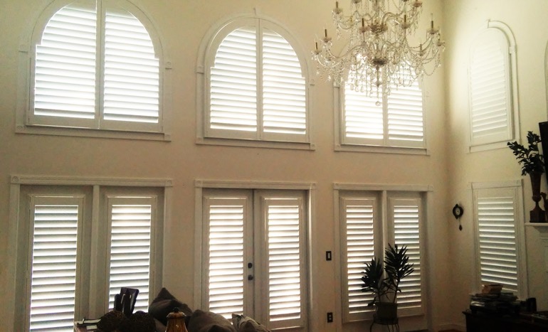 Entertainment room in open concept Boston home with plantation shutters on arch windows.