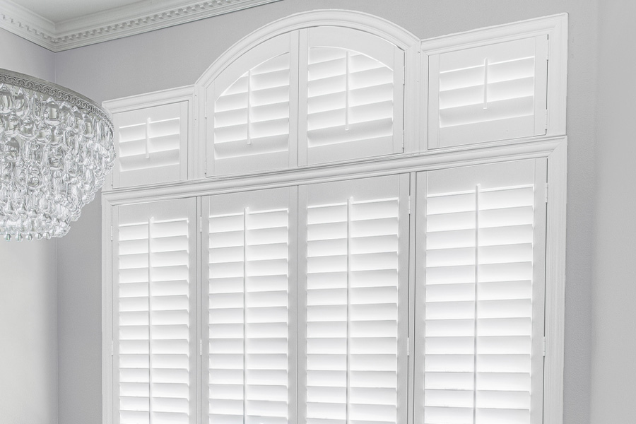 Custom interior shutters fit every window, even the most beautiful specialty shaped ones. White Polywood shutters in a gray dining room