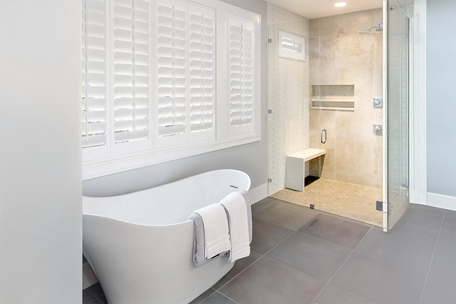 White Polywood shutters on a large window over a freestanding tub